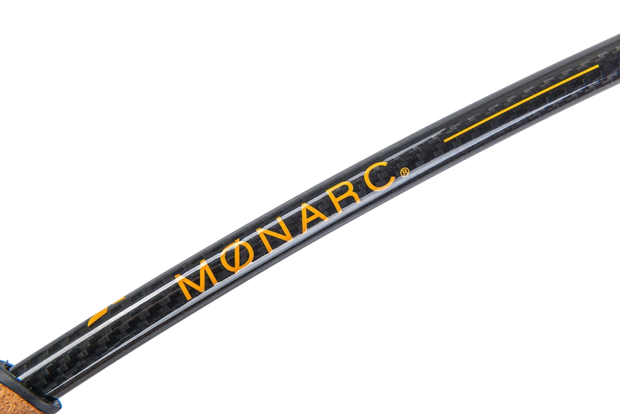 Logo monarc visible sur un bâton de marche orange sur fond de fibres de carbone